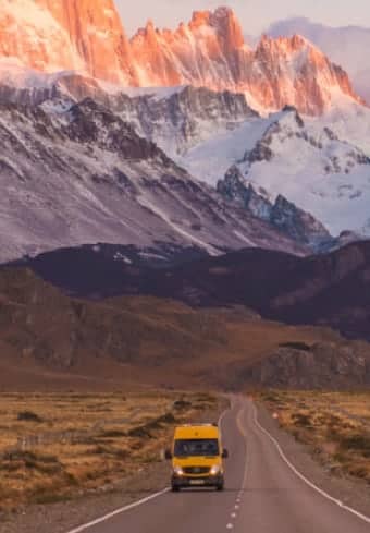 Żółty kamper na otwartej drodze pod pokrytym śniegiem masywem Fitz Roy w Patagonii